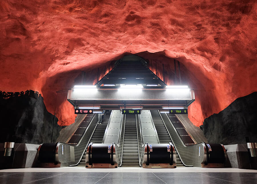 O statie de metrou portocalie asemanatoare unei pesteri, Statia Solna Centrum din Stockholm, cu o banca de scari rulante.
