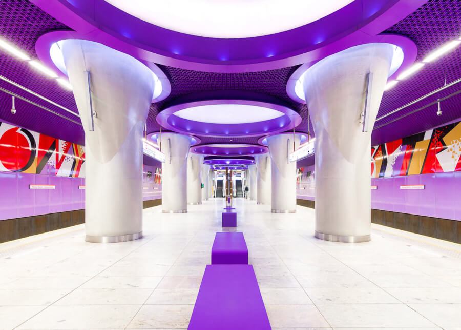O statie de metrou ultra moderna din Varsovia, cu un acoperis mov, coloane in forma si poze colorate pe pereti.