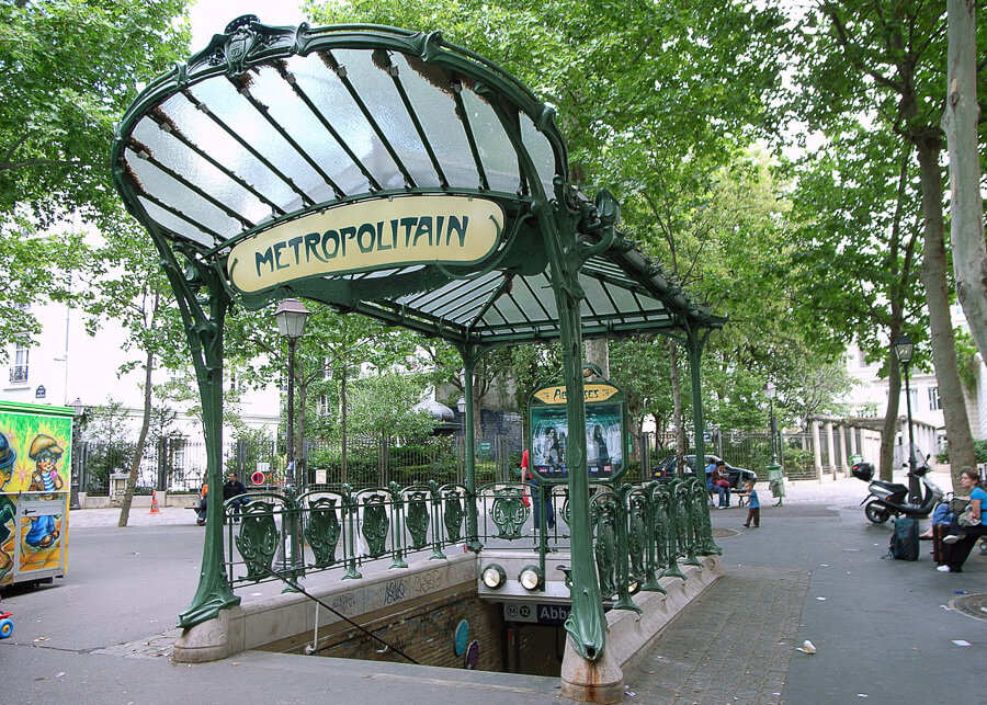 Exteriorul unei statii de metrou din Paris, cu fier forjat verde si un panou pe care scrie „Metropolitain”.