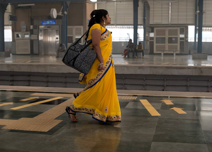O femeie in sari galben se plimba de-a lungul peronului unei frumoase statii de metrou din Delhi.