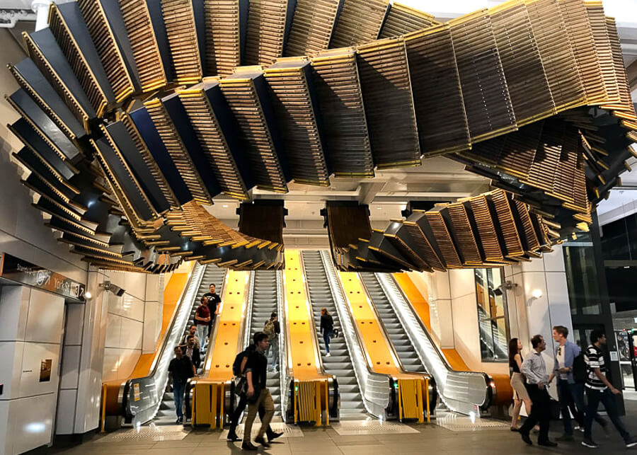 Un set de scari rulante cu o sculptura neobisnuita din lemn atarnand de sus la statia Wynyard din Sydney.