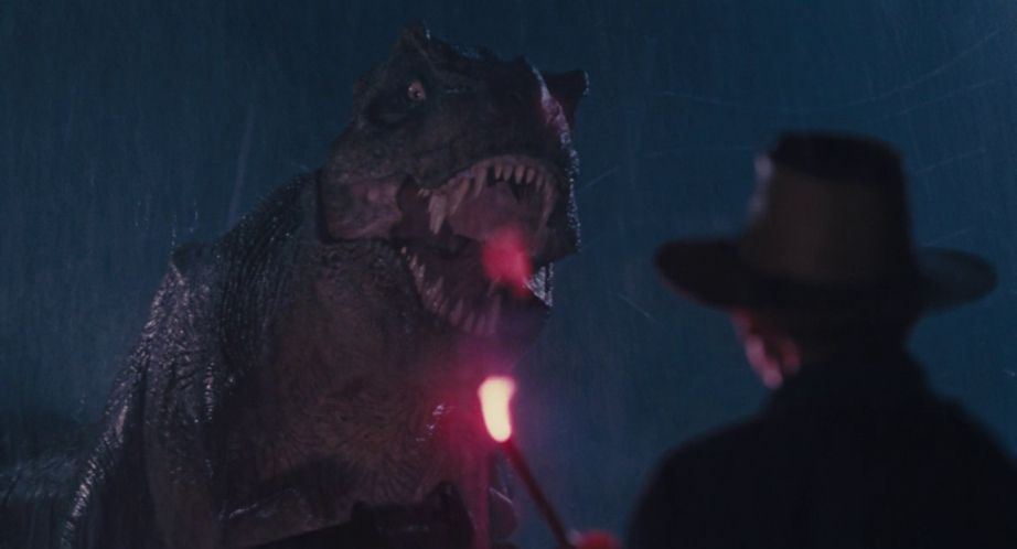 Un barbat care poarta o palarie tine o racheta de lumina in fata unui tiranozaur rex care urla in Jurassic Park.