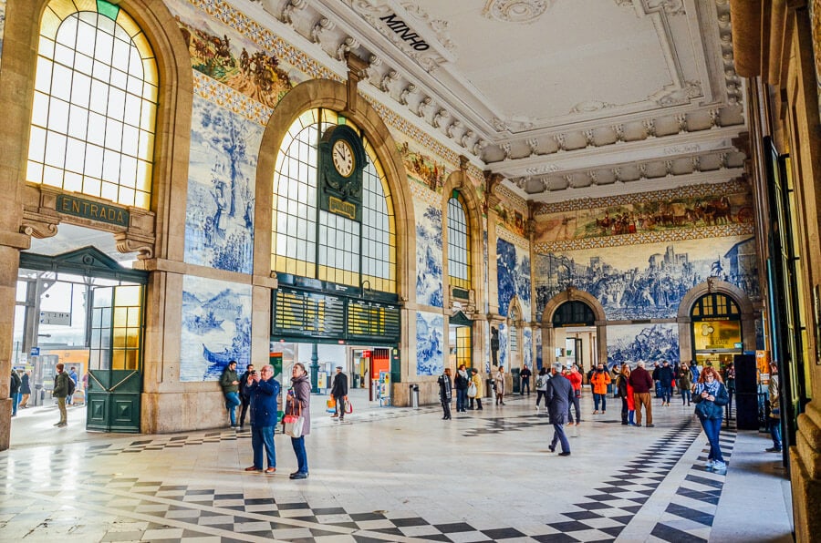 Oamenii trec pe langa o pictura murala cu faianta albastra si alba din statia de metrou si cale ferata Sao Bento din Porto, Portugalia.