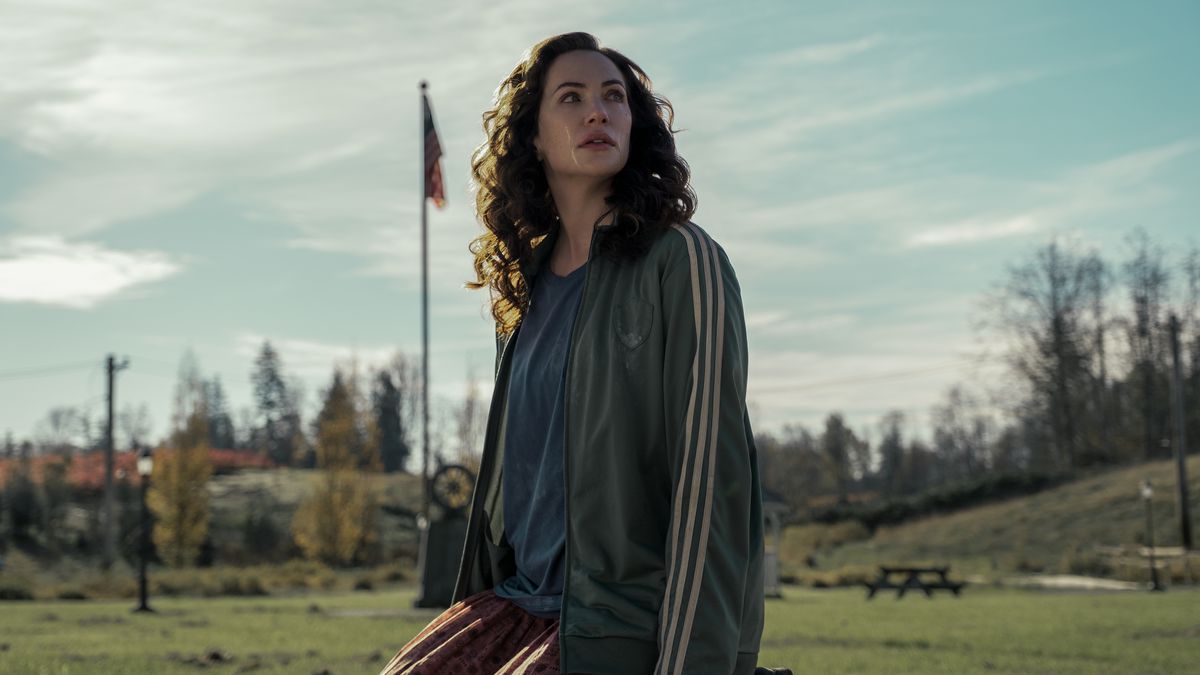 Kate Siegel se uita spre stanga in timp ce sta pe un gard in cadrul Liturghiei de la miezul noptii. Un steag american apare in spatele ei.